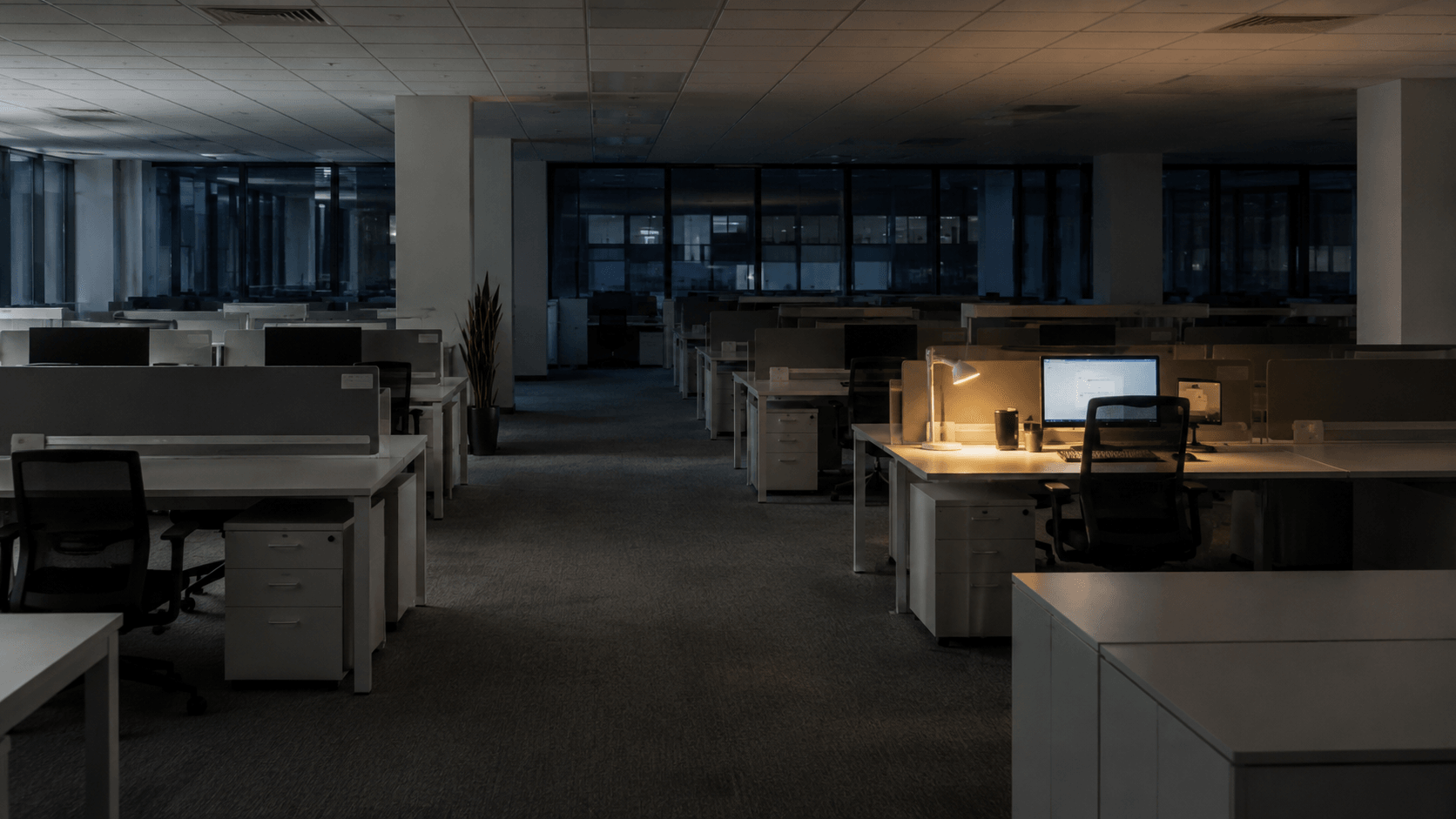 Nearly empty modern office with one active workstation glowing softly